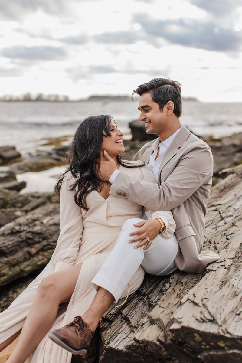 a couple sitting on a boulder at Kettle Cove by the water at sunset.